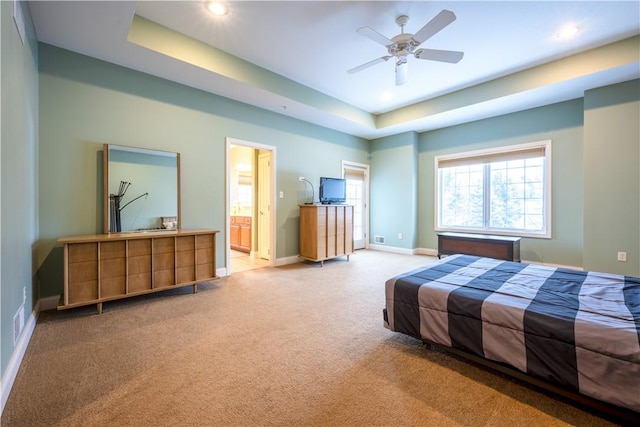 bedroom featuring ceiling fan, a tray ceiling, ensuite bath, and carpet flooring