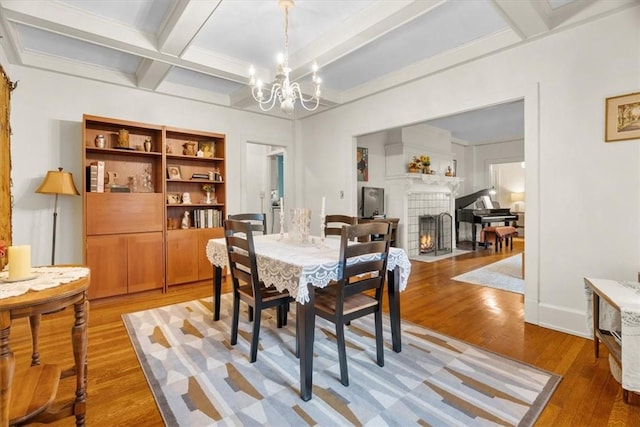 dining room with coffered ceiling, a notable chandelier, a fireplace, wood-type flooring, and beamed ceiling