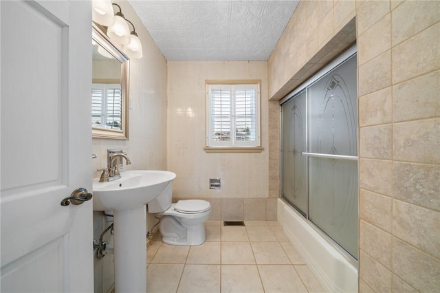 full bathroom with sink, tile walls, shower / bath combination with glass door, tile patterned flooring, and toilet