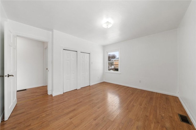 unfurnished bedroom featuring hardwood / wood-style flooring and two closets