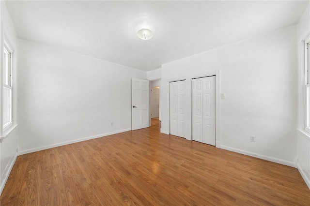 unfurnished bedroom featuring multiple windows, two closets, and light hardwood / wood-style flooring