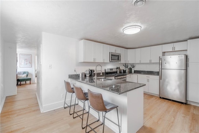 kitchen with appliances with stainless steel finishes, white cabinets, kitchen peninsula, and sink