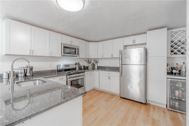 kitchen with stainless steel appliances, white cabinetry, dark stone counters, and sink