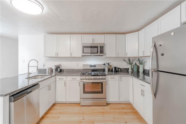 kitchen with dark stone countertops, kitchen peninsula, sink, white cabinetry, and stainless steel appliances