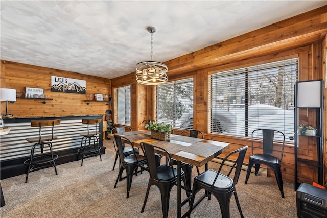 carpeted dining room featuring a wealth of natural light, wood walls, and an inviting chandelier