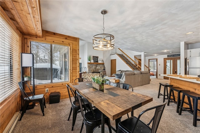 carpeted dining area featuring baseboard heating, a fireplace, wood walls, and a notable chandelier