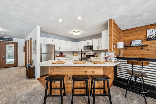 kitchen featuring light carpet, wood walls, a breakfast bar area, appliances with stainless steel finishes, and a center island