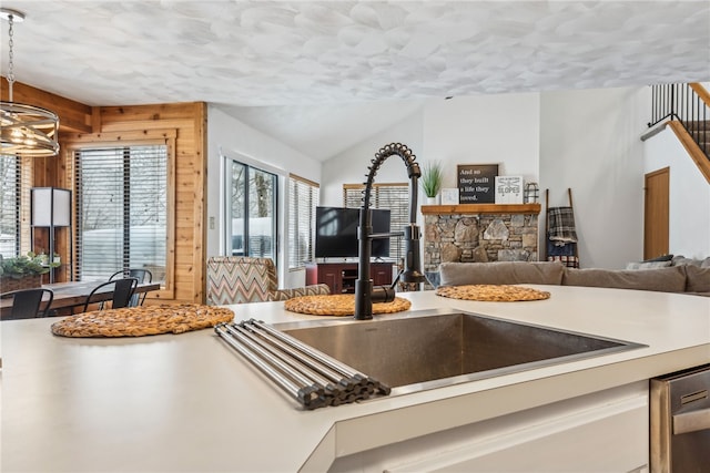 kitchen with dishwasher, a fireplace, wood walls, pendant lighting, and sink