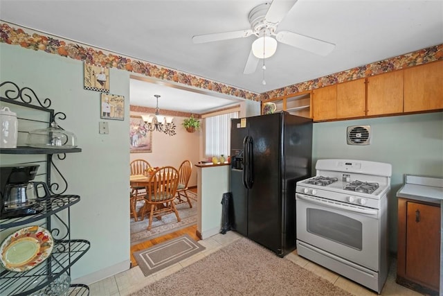 kitchen featuring black refrigerator with ice dispenser, hanging light fixtures, white gas stove, light tile patterned floors, and ceiling fan with notable chandelier