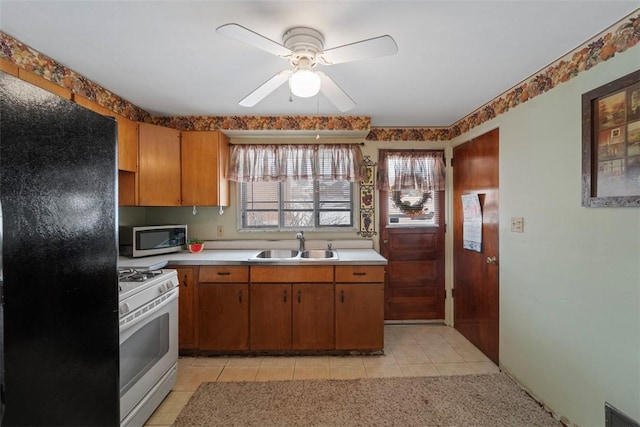 kitchen with sink, black fridge, ceiling fan, white range with gas stovetop, and light tile patterned floors