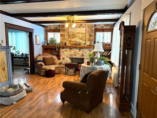 living room featuring radiator heating unit, a fireplace, hardwood / wood-style flooring, ceiling fan, and beam ceiling