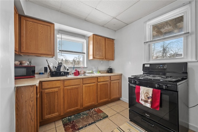 kitchen with sink, a drop ceiling, light tile patterned floors, and black gas range