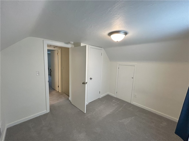 additional living space featuring vaulted ceiling, a textured ceiling, and dark colored carpet