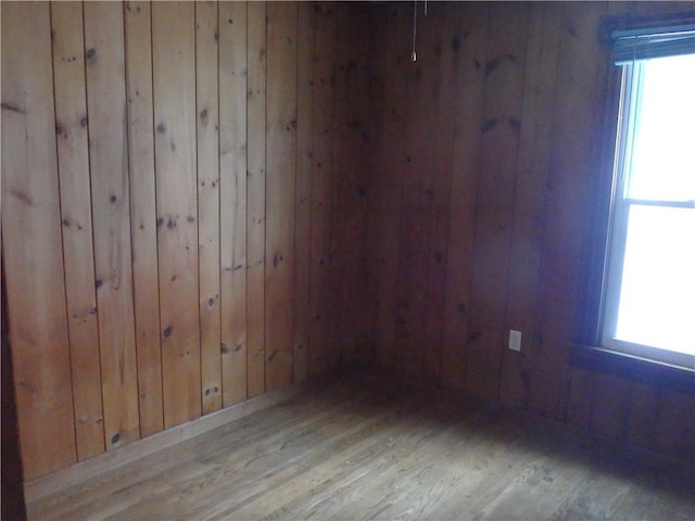 unfurnished room with a healthy amount of sunlight, light hardwood / wood-style flooring, and wood walls