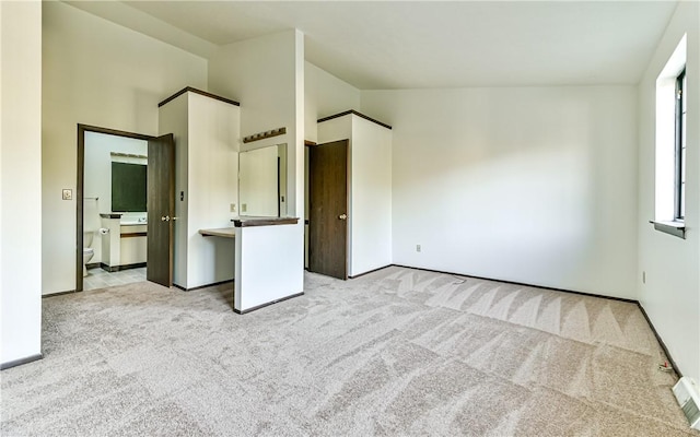 unfurnished bedroom featuring high vaulted ceiling, light colored carpet, and connected bathroom