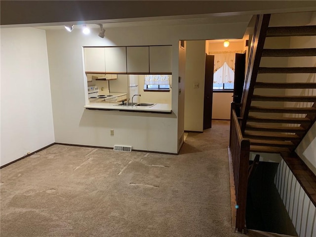 kitchen with track lighting, white cabinetry, white electric stove, sink, and light colored carpet