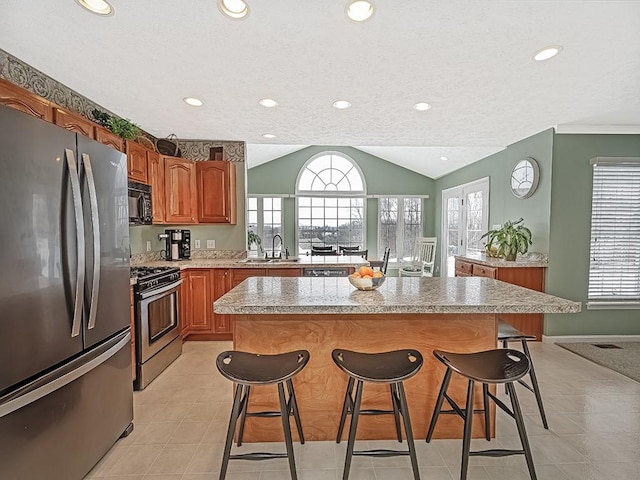 kitchen featuring vaulted ceiling, appliances with stainless steel finishes, a kitchen bar, and a kitchen island