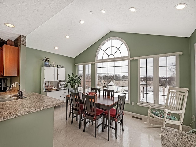 dining space with light tile patterned flooring, sink, a textured ceiling, and vaulted ceiling