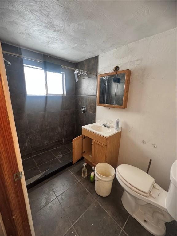 bathroom featuring a textured ceiling, toilet, vanity, and a tile shower