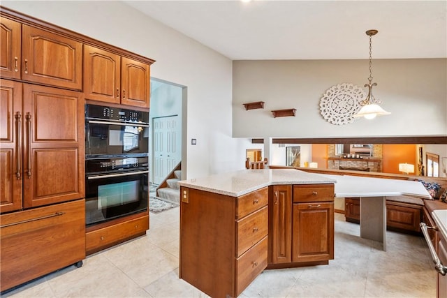 kitchen featuring decorative light fixtures, black double oven, light stone counters, and a center island