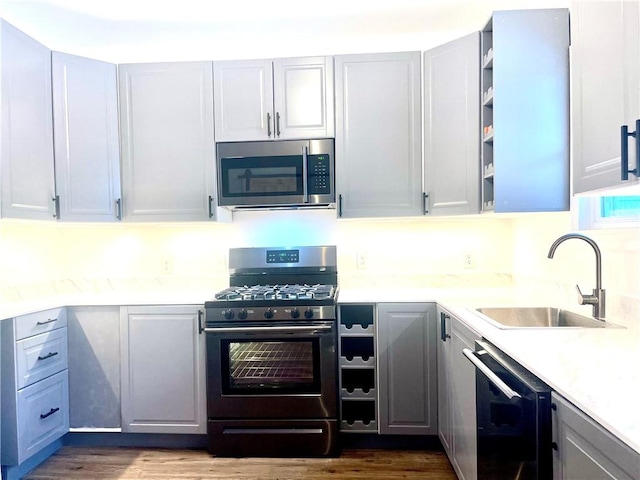 kitchen with appliances with stainless steel finishes, gray cabinetry, hardwood / wood-style floors, and sink