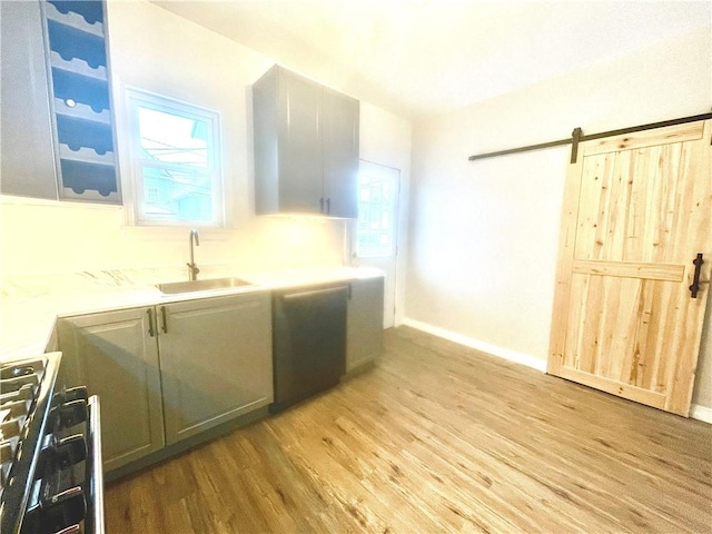 kitchen featuring a barn door, sink, stainless steel range with gas stovetop, light hardwood / wood-style flooring, and light stone counters