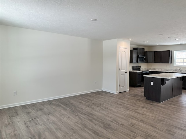 kitchen with a textured ceiling, a kitchen island, stainless steel appliances, light hardwood / wood-style flooring, and a breakfast bar area