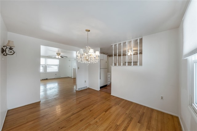 unfurnished dining area with ceiling fan with notable chandelier and wood-type flooring