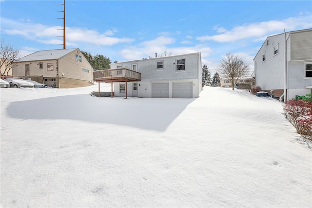 snow covered rear of property with a garage and a wooden deck