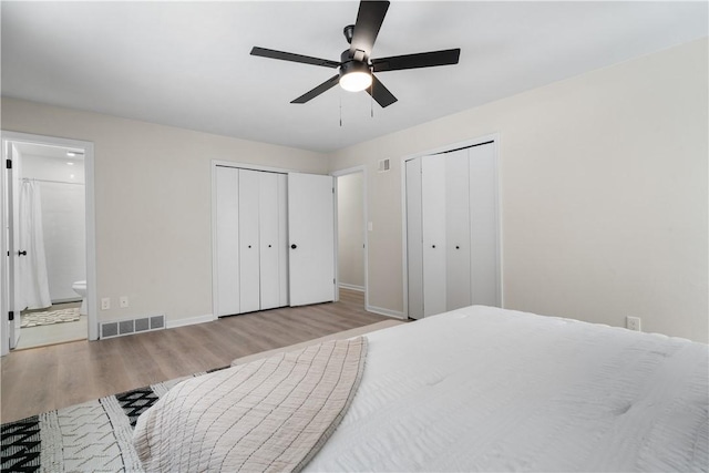 bedroom with light wood-type flooring, ceiling fan, ensuite bathroom, and two closets