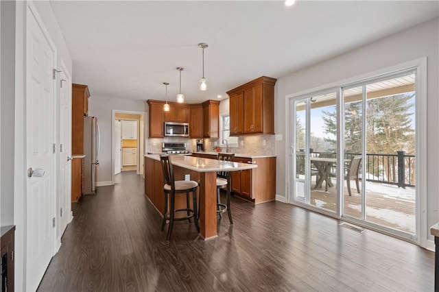 kitchen with a center island, a breakfast bar, hanging light fixtures, dark wood-type flooring, and stainless steel appliances