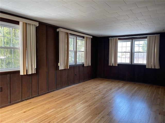 empty room with plenty of natural light, light hardwood / wood-style flooring, and wood walls