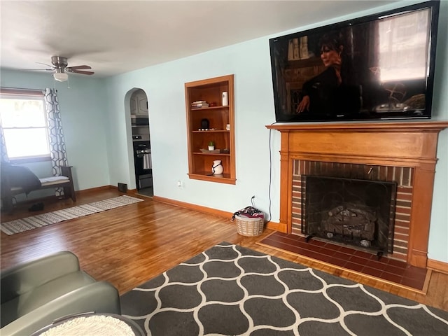 living room featuring ceiling fan, a fireplace, dark hardwood / wood-style flooring, and built in shelves