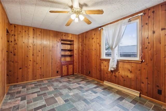 empty room with ceiling fan, baseboard heating, and wood walls