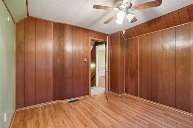 unfurnished room featuring vaulted ceiling, ceiling fan, light hardwood / wood-style floors, and wooden walls