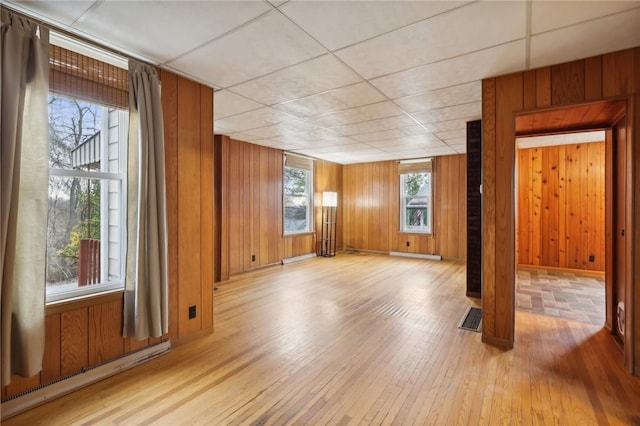 interior space featuring baseboard heating, a drop ceiling, and wooden walls