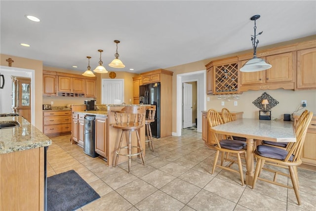 kitchen with an island with sink, hanging light fixtures, black fridge, light stone counters, and light tile patterned floors