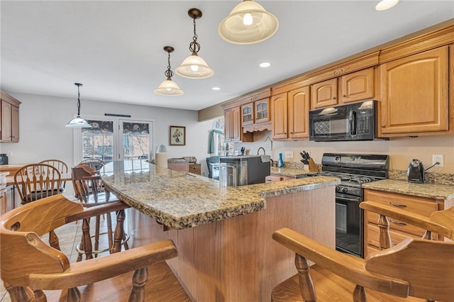 kitchen with decorative light fixtures, light hardwood / wood-style floors, light stone counters, and black appliances