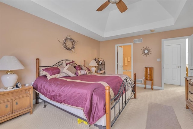 bedroom with ceiling fan, ensuite bathroom, a raised ceiling, and light carpet