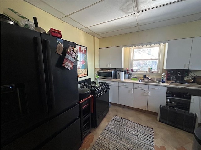 kitchen featuring black appliances, white cabinets, a drop ceiling, and sink