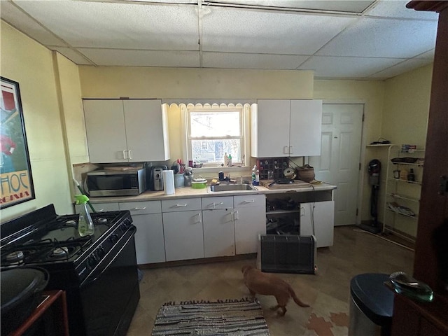 kitchen with sink, a paneled ceiling, black gas stove, and white cabinetry