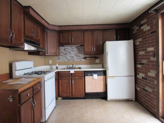 kitchen with brick wall, sink, white appliances, and dark brown cabinets