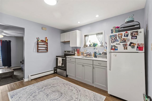 kitchen with white fridge, sink, stainless steel range with electric cooktop, white cabinets, and a baseboard radiator