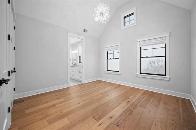 unfurnished bedroom with multiple windows, ensuite bath, a chandelier, and light wood-type flooring