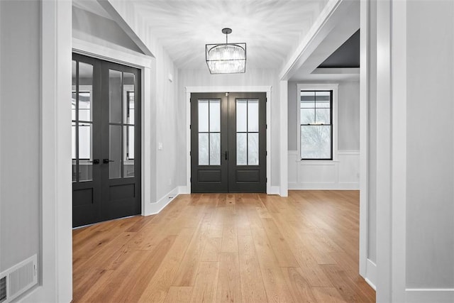 entrance foyer featuring light hardwood / wood-style flooring, french doors, and a notable chandelier