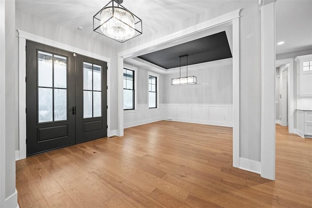 foyer entrance featuring light hardwood / wood-style floors, plenty of natural light, a raised ceiling, french doors, and a chandelier