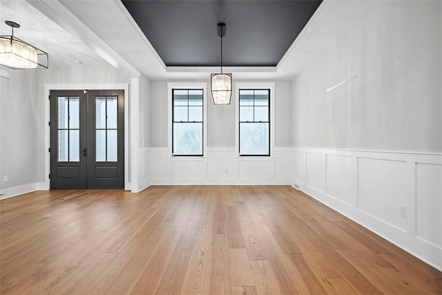 foyer with light wood-type flooring, a raised ceiling, french doors, and a notable chandelier