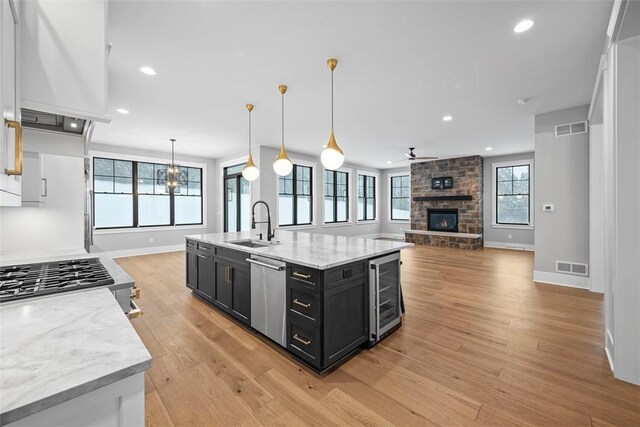 kitchen with wine cooler, decorative light fixtures, dishwasher, a kitchen island with sink, and light stone countertops