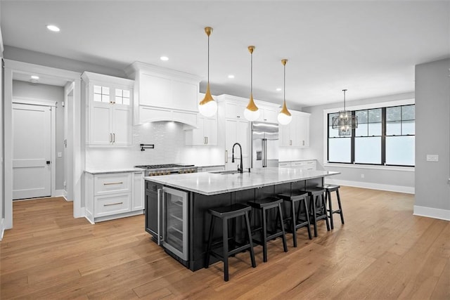 kitchen featuring built in refrigerator, decorative light fixtures, white cabinetry, and a center island with sink