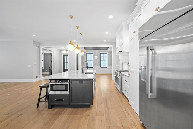 kitchen with pendant lighting, white cabinetry, light wood-type flooring, a kitchen island with sink, and high quality appliances